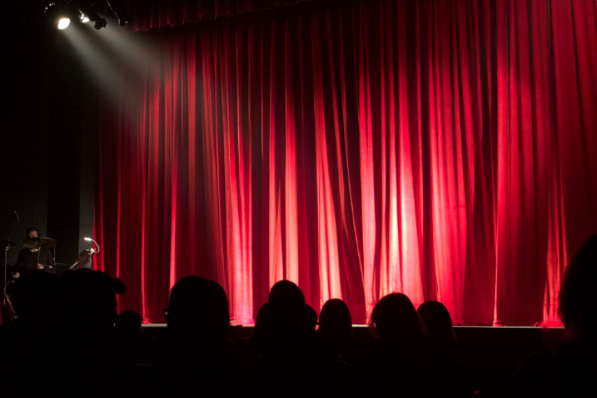 Concert stage with red curtain, spotlights, and audience.
