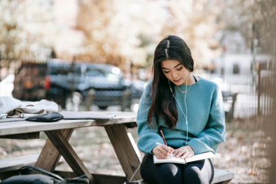 Music student studying outdoors with notepad and headphones.